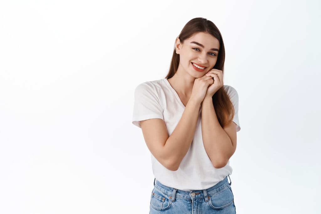 tender lovely girl hold hands near cheeks, smiling and looking b