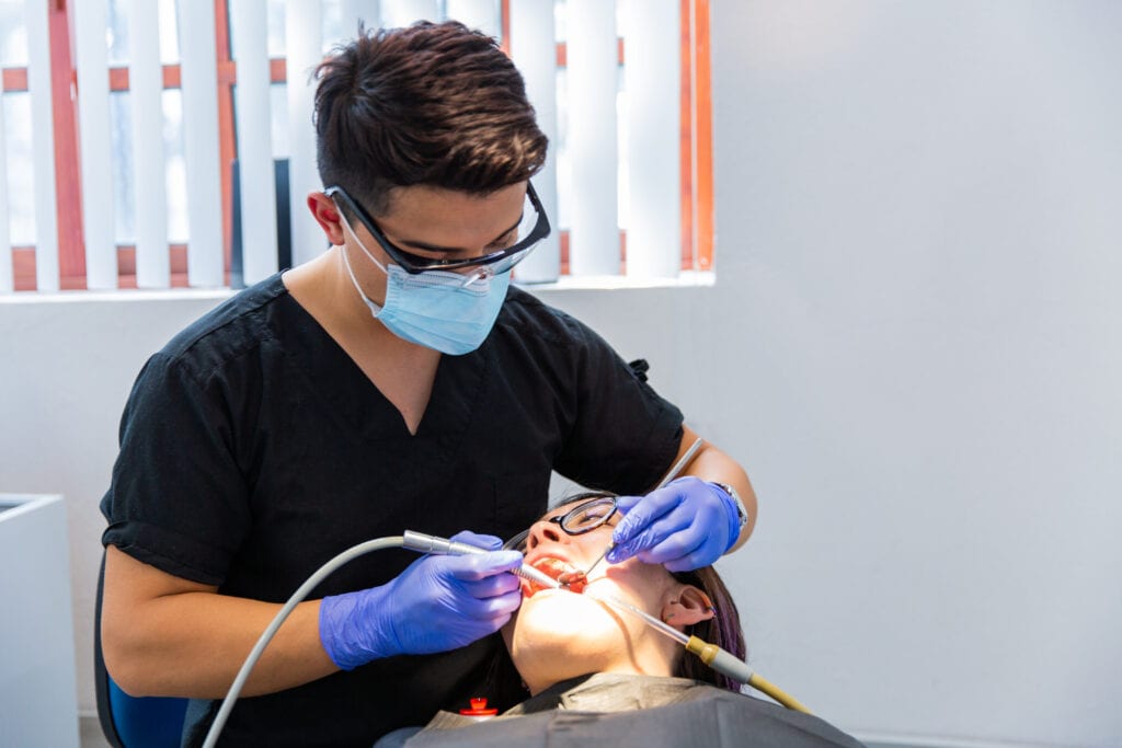 men dentist wearing protective face mask examining a patient.